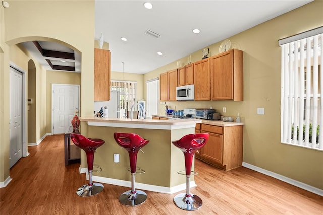 31108 Whitlock Dr, Wesley Chapel, FL 33543 - kitchen with white microwave, a kitchen bar, light wood-style floors, stove, and recessed lighting