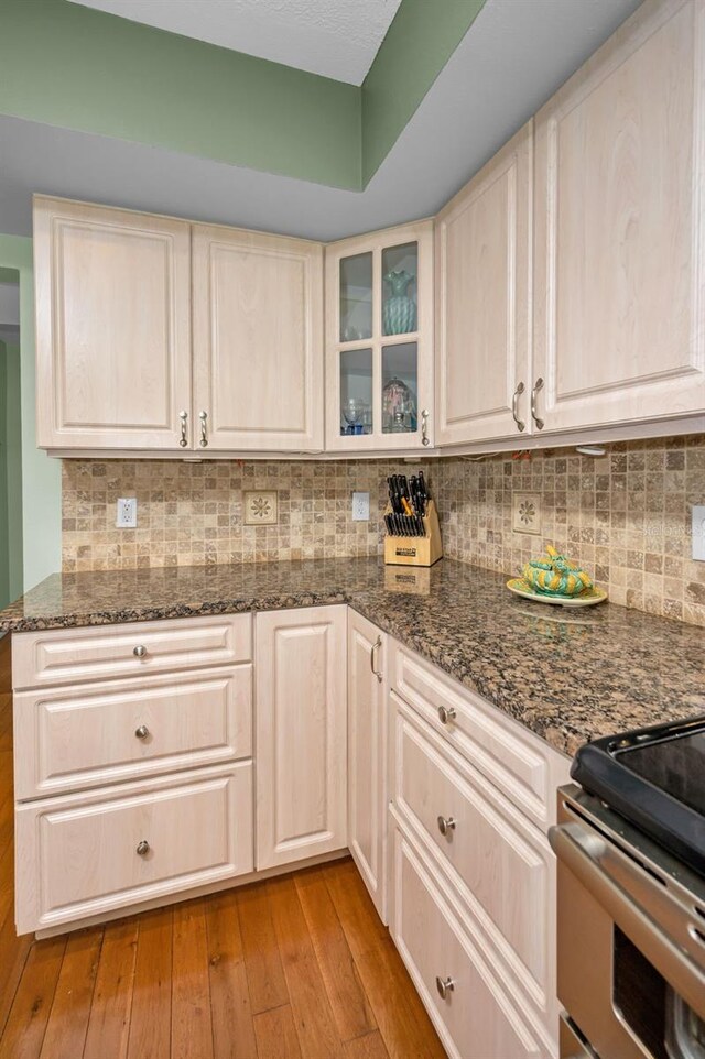 250 Rosery Rd NW Unit 218, Largo, FL 33770 - kitchen featuring light wood-type flooring, decorative backsplash, glass insert cabinets, dark stone counters, and stainless steel range with electric stovetop