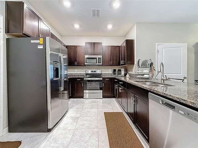 841 Royal Empress Dr, Ruskin, FL 33570 - kitchen featuring appliances with stainless steel finishes, a sink, dark stone countertops, dark brown cabinets, and light tile patterned floors