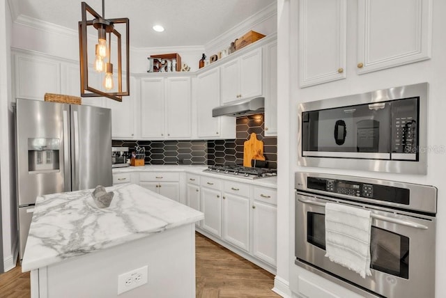 15934 Sorawater Dr, Lithia, FL 33547 - kitchen featuring appliances with stainless steel finishes, under cabinet range hood, ornamental molding, white cabinetry, and tasteful backsplash