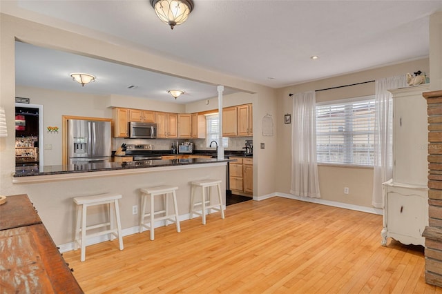 6114 7th Ave S, Gulfport, FL 33707 - kitchen with stainless steel appliances, light wood-style flooring, dark countertops, a breakfast bar, and light brown cabinets