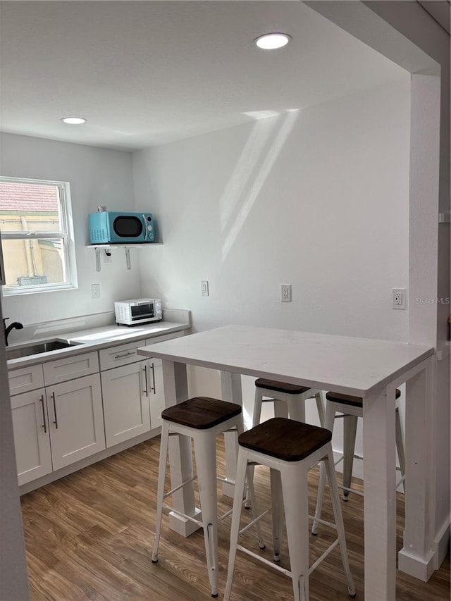 14141 Gulf Blvd Unit 5, Saint Petersburg, FL 33708 - kitchen featuring a sink, wood finished floors, light countertops, a breakfast bar area, and white cabinets