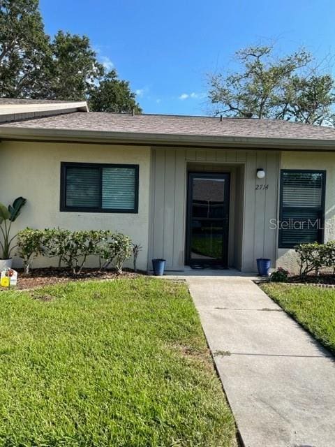 2714 60th Avenue Terrace W Unit 12D, Bradenton, FL 34207 - view of exterior entry featuring board and batten siding, a yard, and a shingled roof