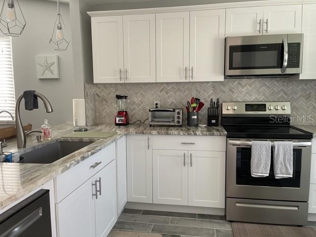2714 60th Avenue Terrace W Unit 12D, Bradenton, FL 34207 - kitchen featuring stainless steel appliances, a sink, white cabinets, decorative backsplash, and light stone countertops
