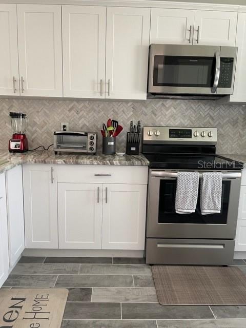 2714 60th Avenue Terrace W Unit 12D, Bradenton, FL 34207 - kitchen featuring appliances with stainless steel finishes, white cabinetry, wood tiled floors, tasteful backsplash, and light stone counters