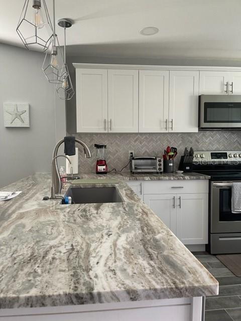 2714 60th Avenue Terrace W Unit 12D, Bradenton, FL 34207 - kitchen featuring appliances with stainless steel finishes, a sink, white cabinetry, light stone counters, and tasteful backsplash