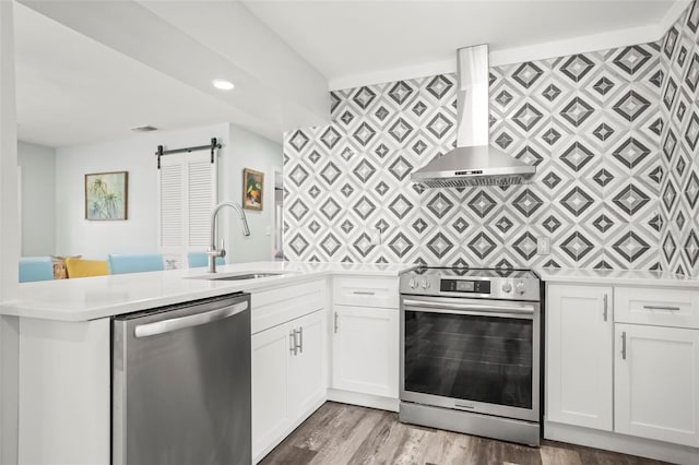 2479 Trade Winds Dr, Dunedin, FL 34698 - kitchen featuring appliances with stainless steel finishes, wall chimney range hood, a sink, a barn door, and a peninsula