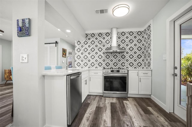 2479 Trade Winds Dr, Dunedin, FL 34698 - kitchen featuring stainless steel appliances, wall chimney range hood, a sink, light countertops, and a barn door