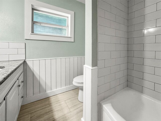 2479 Trade Winds Dr, Dunedin, FL 34698 - full bathroom featuring vanity, toilet, a wainscoted wall, wood finished floors, and shower / washtub combination
