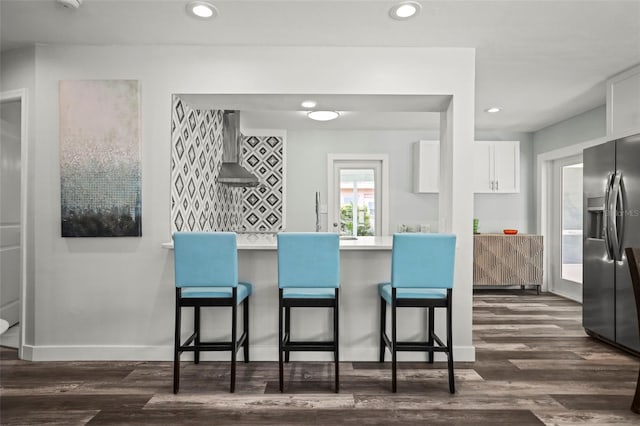2479 Trade Winds Dr, Dunedin, FL 34698 - kitchen featuring stainless steel fridge, wall chimney range hood, a kitchen breakfast bar, white cabinets, and dark wood-type flooring