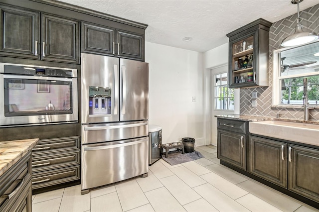 5005 W Evelyn Dr, Tampa, FL 33609 - kitchen featuring appliances with stainless steel finishes, decorative backsplash, glass insert cabinets, decorative light fixtures, and a textured ceiling