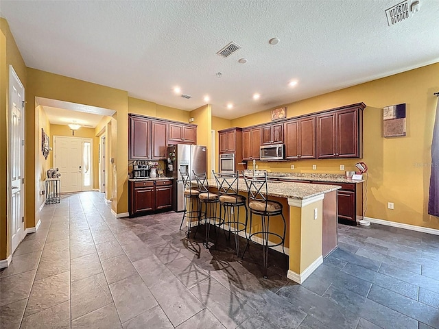 4916 Rolling Green Dr, Wesley Chapel, FL 33543 - kitchen with stainless steel appliances, baseboards, a kitchen island with sink, a kitchen bar, and a textured ceiling