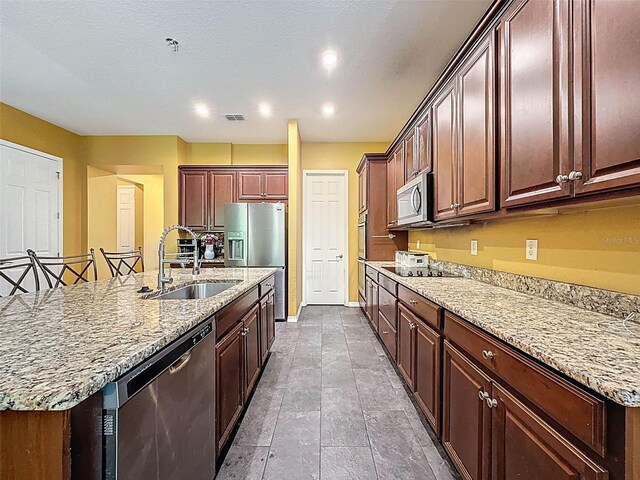 4916 Rolling Green Dr, Wesley Chapel, FL 33543 - kitchen featuring a sink, appliances with stainless steel finishes, a center island with sink, light stone countertops, and baseboards