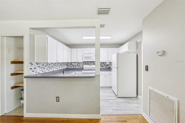 1015 13th Ave NW, Largo, FL 33770 - kitchen featuring white appliances, a peninsula, backsplash, white cabinetry, and dark countertops