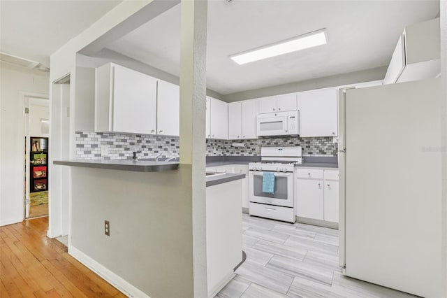 1015 13th Ave NW, Largo, FL 33770 - kitchen featuring white appliances, a peninsula, backsplash, and white cabinets