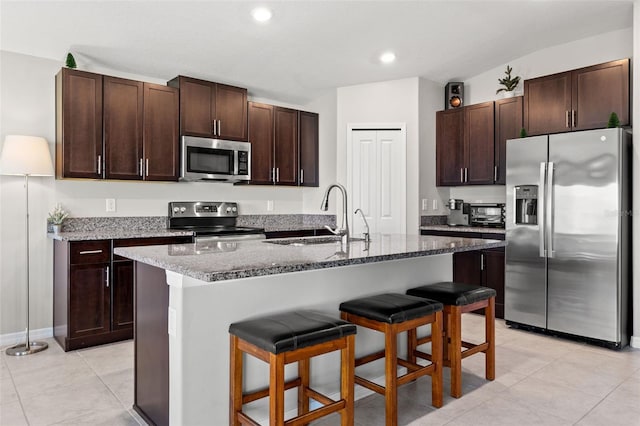 16632 Sunburst Lake St, Wimauma, FL 33598 - kitchen featuring appliances with stainless steel finishes, a sink, a breakfast bar, dark brown cabinetry, and stone countertops