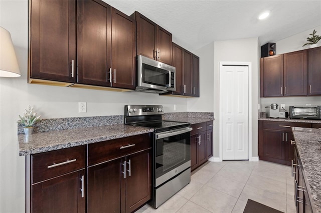 16632 Sunburst Lake St, Wimauma, FL 33598 - kitchen featuring appliances with stainless steel finishes, dark brown cabinetry, light tile patterned floors, dark stone counters, and baseboards