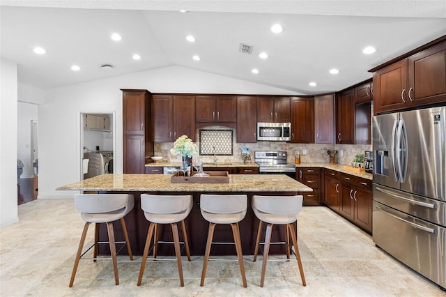 12470 93rd St, Largo, FL 33773 - kitchen featuring stainless steel appliances, washer and clothes dryer, vaulted ceiling, a center island with sink, and a kitchen bar