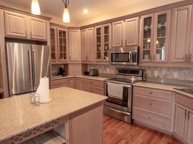 101 8th St, Belleair Beach, FL 33786 - kitchen featuring appliances with stainless steel finishes, light wood finished floors, pendant lighting, tasteful backsplash, and glass insert cabinets