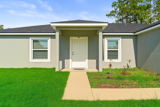7839 N Quibble Ave, Citrus Springs, FL 34434 - view of exterior entry featuring a lawn, stucco siding, and roof with shingles