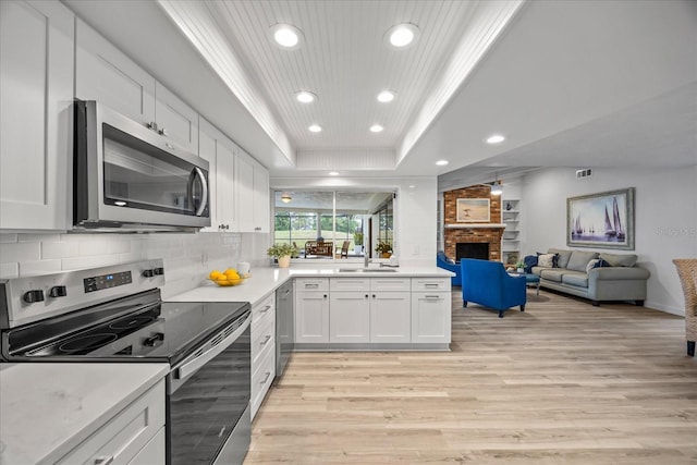 2900 Sandpiper Pl, Clearwater, FL 33762 - kitchen with stainless steel appliances, a tray ceiling, recessed lighting, light wood-style floors, and a brick fireplace