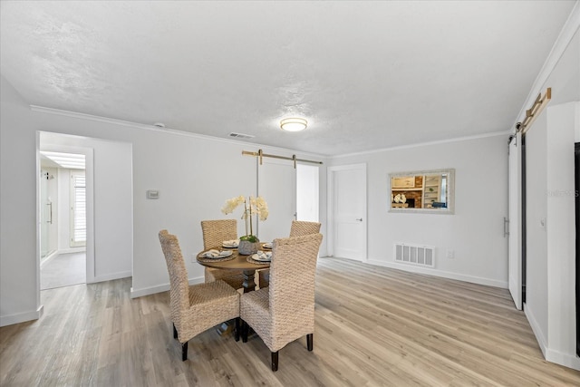 2900 Sandpiper Pl, Clearwater, FL 33762 - dining space with a barn door, light wood-style flooring, baseboards, crown molding, and a textured ceiling