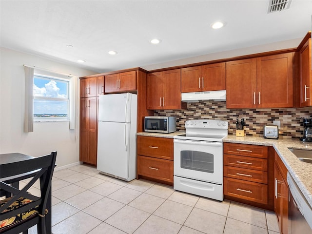 13500 Gulf Blvd Unit 506, Madeira Beach, FL 33708 - kitchen with stainless steel appliances, under cabinet range hood, brown cabinets, backsplash, and light tile patterned flooring