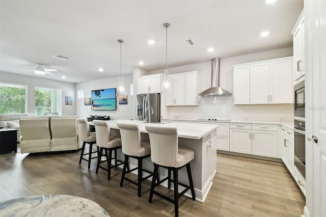 527 Bay St, Dunedin, FL 34698 - kitchen with wall chimney exhaust hood, stainless steel appliances, open floor plan, light countertops, and light wood-style flooring