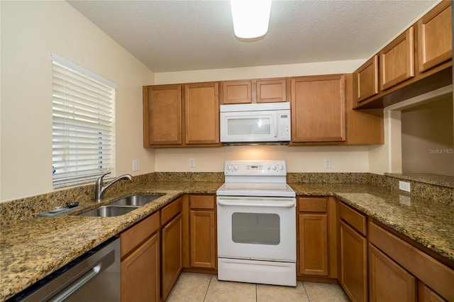 37712 Aaralyn Rd, Zephyrhills, FL 33542 - kitchen with white appliances, a sink, brown cabinets, dark stone counters, and a textured ceiling