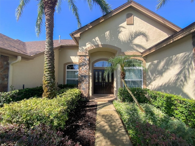 2041 Gold Dust Ct, Trinity, FL 34655 - view of exterior entry featuring stucco siding, french doors, stone siding, and a shingled roof