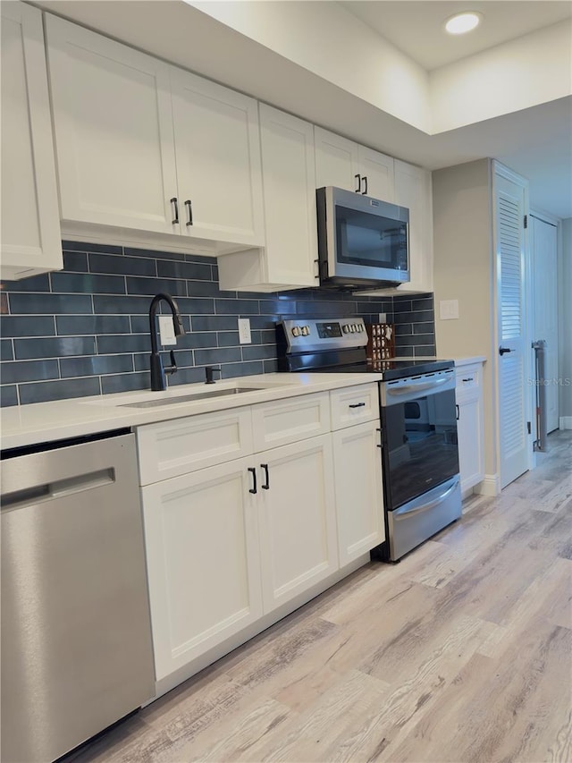 30 Tads Trl, Oldsmar, FL 34677 - kitchen with stainless steel appliances, a sink, light wood-style flooring, white cabinetry, and light countertops