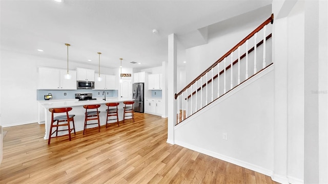 9293 Rally Spring Loop, Wesley Chapel, FL 33545 - kitchen featuring stainless steel appliances, a kitchen breakfast bar, light countertops, light wood finished floors, and white cabinets