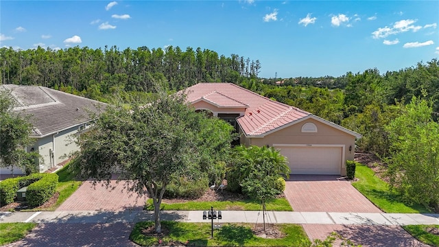 15860 Aurora Lake Cir, Wimauma, FL 33598 - view of front facade featuring a tile roof, stucco siding, an attached garage, decorative driveway, and a forest view