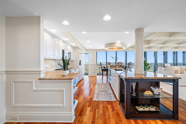 7600 Bayshore Dr Unit 1201A, Treasure Island, FL 33706 - kitchen featuring stainless steel microwave, white cabinetry, decorative columns, light wood-type flooring, and a decorative wall