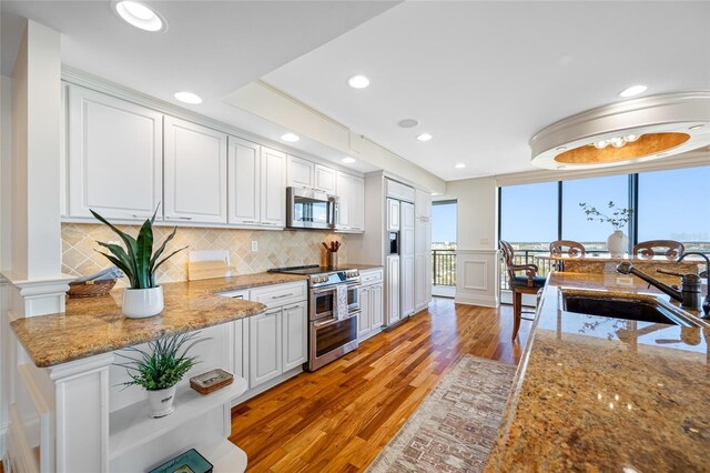 7600 Bayshore Dr Unit 1201A, Treasure Island, FL 33706 - kitchen featuring stainless steel appliances, a sink, light wood-style floors, backsplash, and white cabinetry