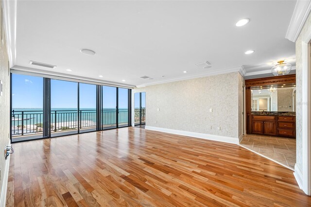 7600 Bayshore Dr Unit 1201A, Treasure Island, FL 33706 - spare room featuring light wood-style floors, crown molding, a water view, a wall of windows, and baseboards