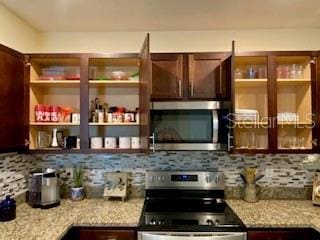 1398 Crescent Hoop Way, Wesley Chapel, FL 33543 - kitchen with appliances with stainless steel finishes, decorative backsplash, dark brown cabinetry, and light stone countertops