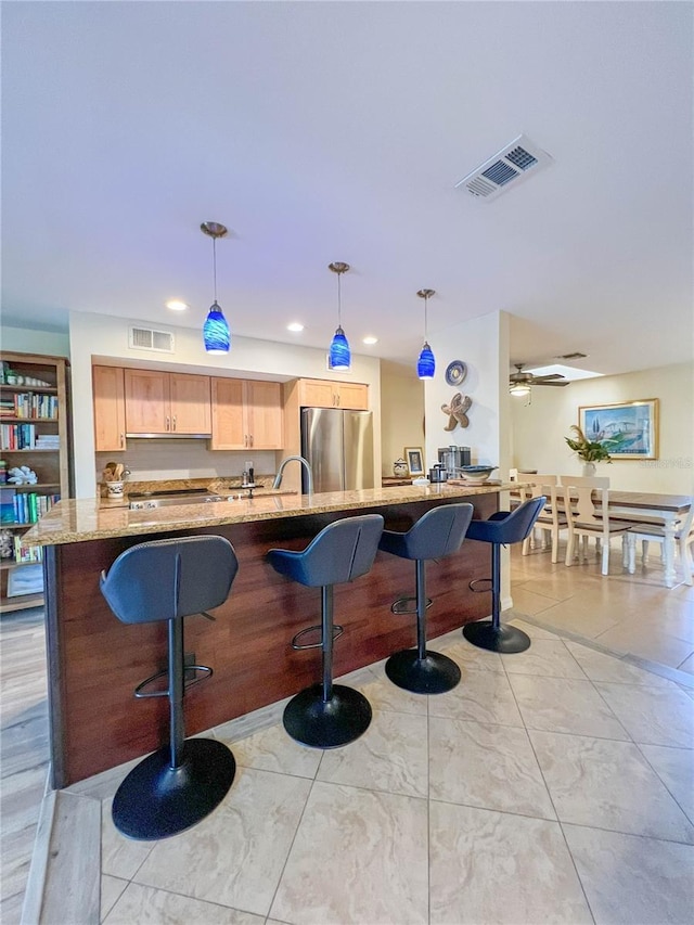 659 Garland Cir, Indian Rocks Beach, FL 33785 - kitchen with stainless steel appliances, light brown cabinets, light stone countertops, a kitchen breakfast bar, and pendant lighting