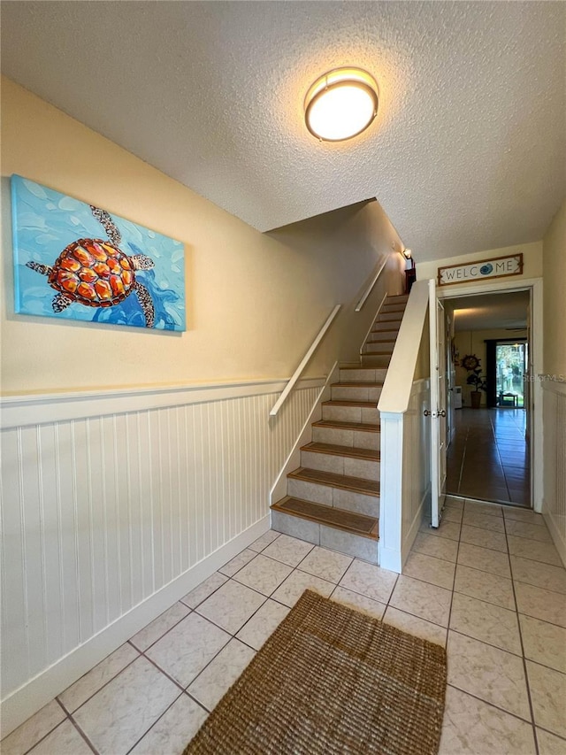 659 Garland Cir, Indian Rocks Beach, FL 33785 - stairs with a wainscoted wall, tile patterned flooring, a textured ceiling, and baseboards