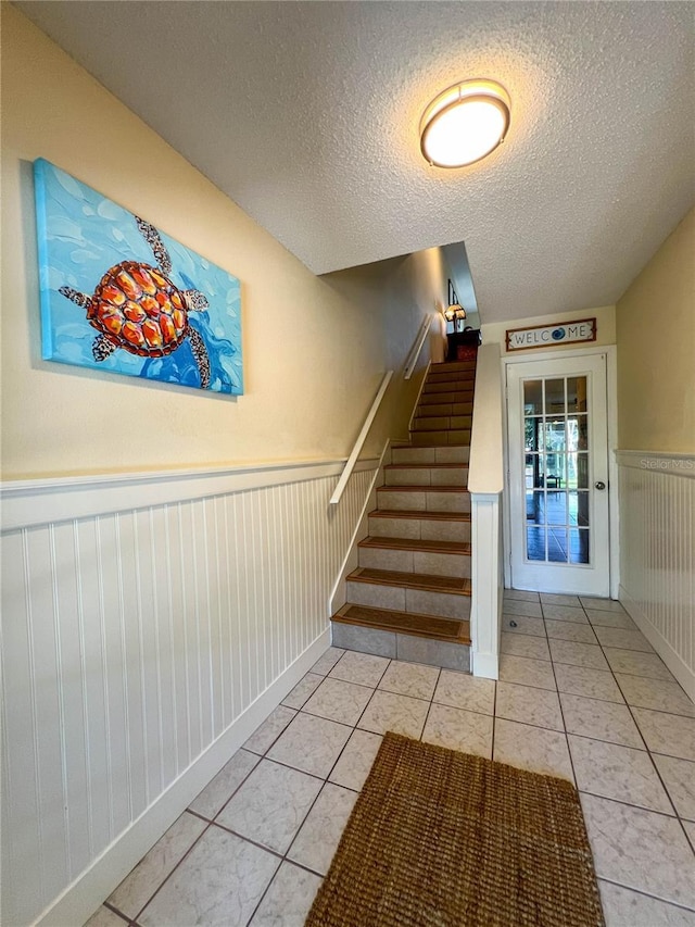 659 Garland Cir, Indian Rocks Beach, FL 33785 - staircase with wainscoting, a textured ceiling, and tile patterned floors