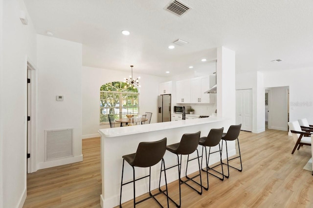970 Ridgewood Ter, Tarpon Springs, FL 34689 - kitchen featuring stainless steel fridge with ice dispenser, white cabinets, a kitchen breakfast bar, a peninsula, and light countertops
