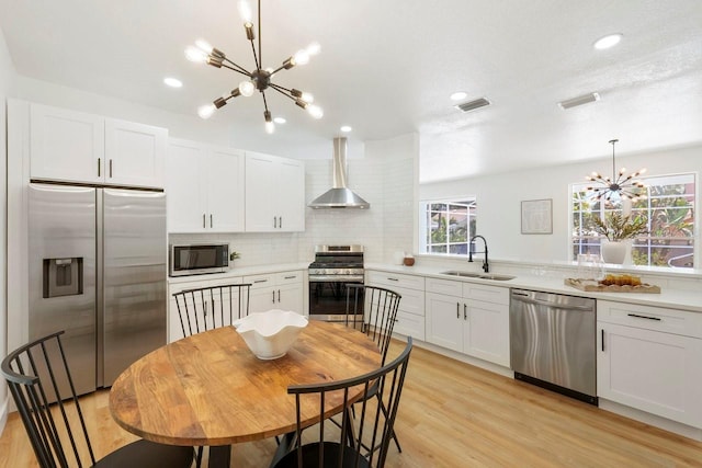 970 Ridgewood Ter, Tarpon Springs, FL 34689 - kitchen featuring stainless steel appliances, a chandelier, wall chimney range hood, a sink, and white cabinetry