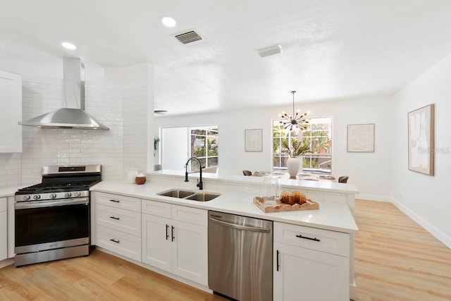 970 Ridgewood Ter, Tarpon Springs, FL 34689 - kitchen featuring appliances with stainless steel finishes, wall chimney exhaust hood, a sink, a peninsula, and a chandelier