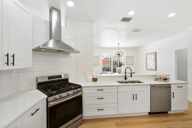 970 Ridgewood Ter, Tarpon Springs, FL 34689 - kitchen with appliances with stainless steel finishes, wall chimney exhaust hood, a sink, white cabinets, and light wood-style flooring