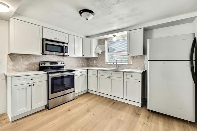 11130 White Oak Ln, Port Richey, FL 34668 - kitchen featuring stainless steel appliances, a sink, light wood finished floors, light countertops, and white cabinets