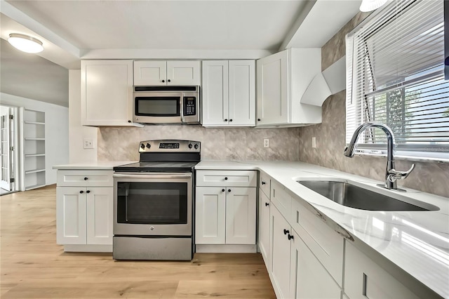 11130 White Oak Ln, Port Richey, FL 34668 - kitchen featuring appliances with stainless steel finishes, a sink, white cabinetry, light wood finished floors, and tasteful backsplash