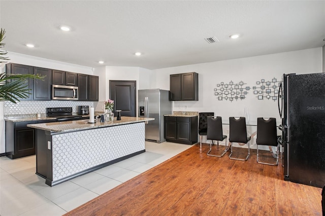 10233 Opaline Sky Pl, Riverview, FL 33578 - kitchen with black appliances, light stone counters, decorative backsplash, an island with sink, and recessed lighting