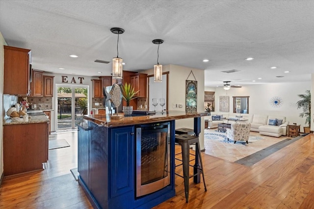 4301 S Lockwood Ridge Rd, Sarasota, FL 34231 - kitchen with wine cooler, light wood-type flooring, a textured ceiling, a kitchen breakfast bar, and decorative backsplash