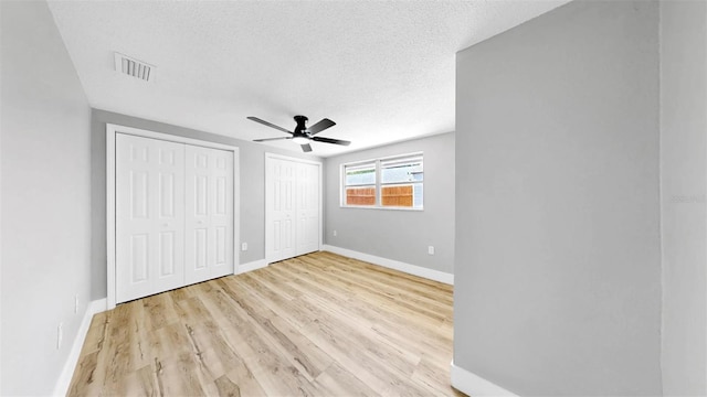 829 Riverside Dr, Tarpon Springs, FL 34689 - unfurnished bedroom with two closets, baseboards, light wood-style floors, a textured ceiling, and a ceiling fan