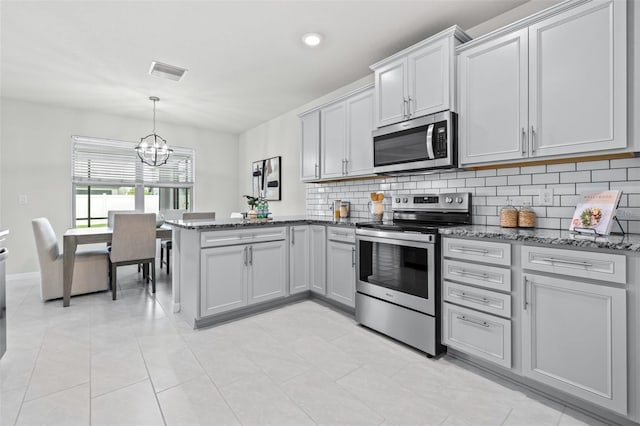6563 Ryestone Way, Wesley Chapel, FL 33545 - kitchen with stainless steel appliances, a peninsula, a chandelier, decorative backsplash, and dark stone countertops
